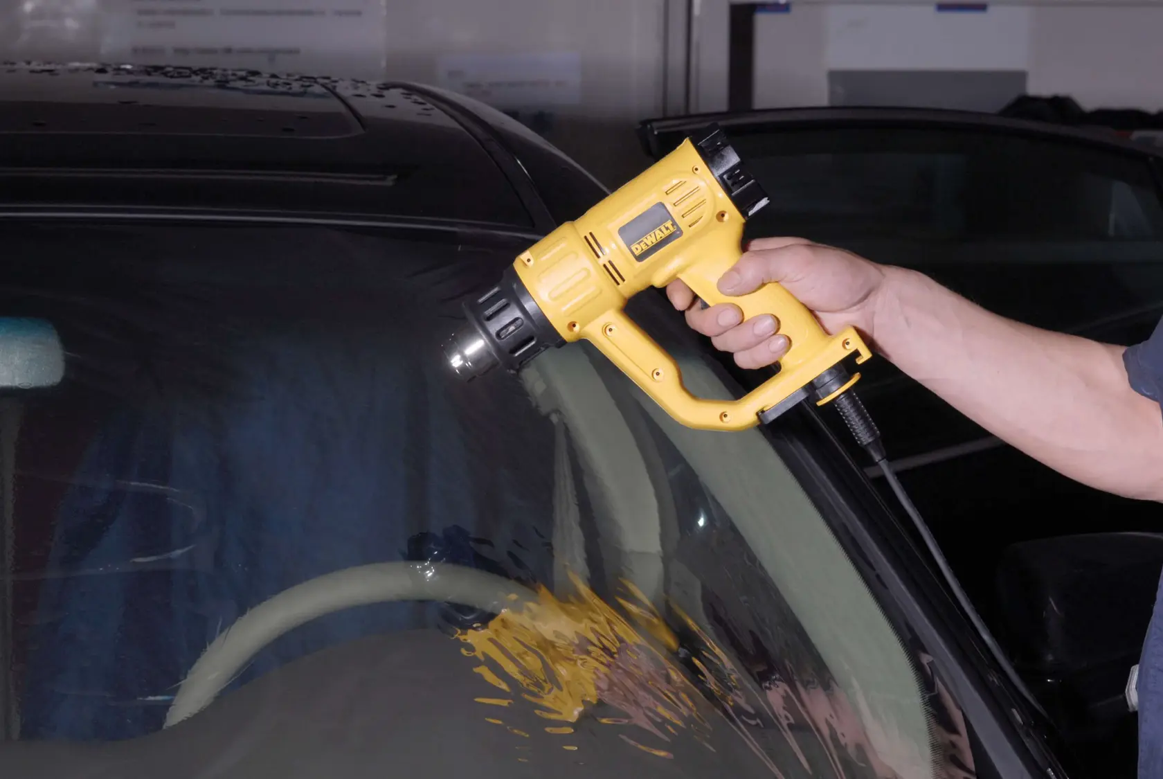 Eine Person verwendet eine Heißluftpistole von DEWALT (Modell D26411), um Hitze auf die Windschutzscheibe eines Autos aufzutragen.
