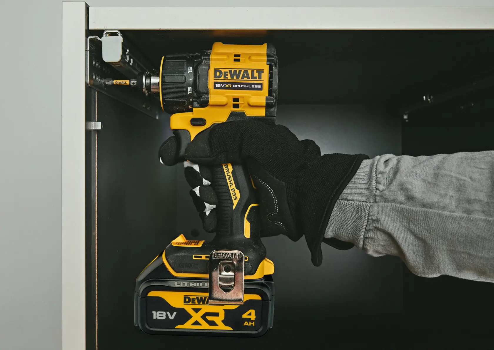Gloved hand using a DEWALT 18V XR brushless drill inside a cabinet for assembly.