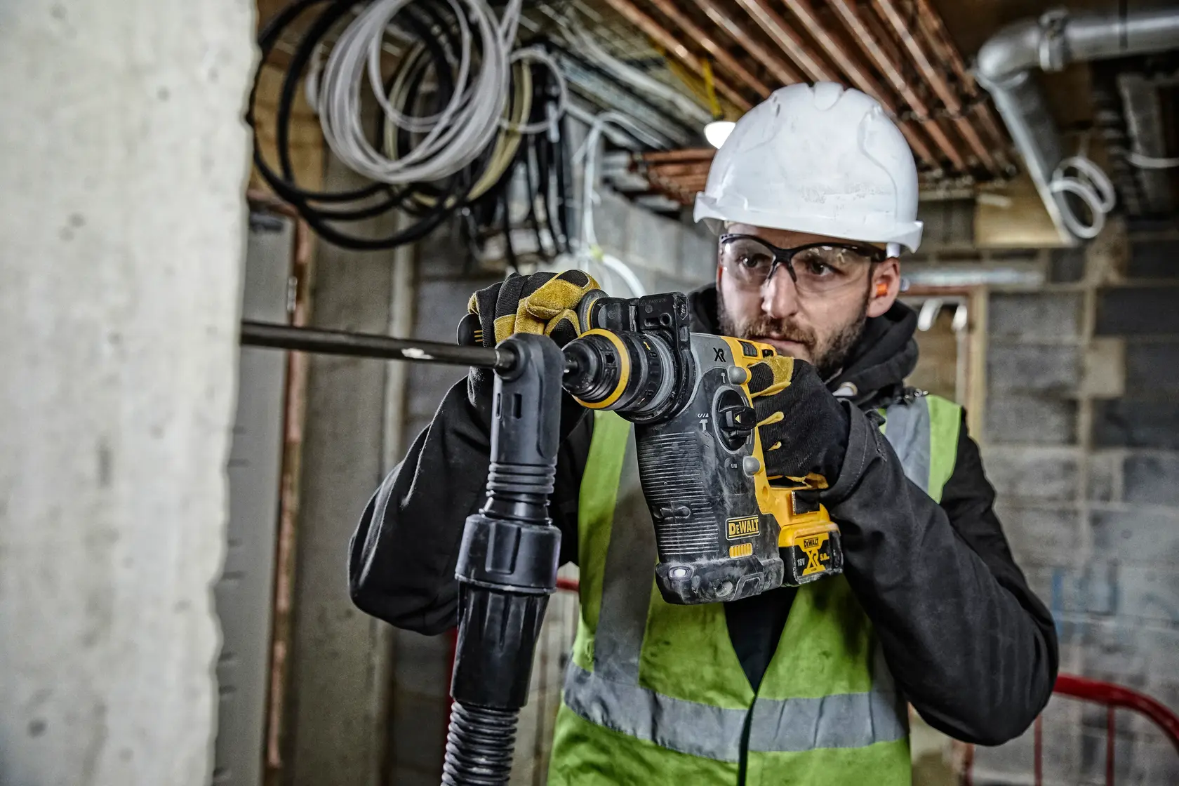 Worker in safety gear using a DEWALT DCH274P2T rotary hammer drill on a construction site.