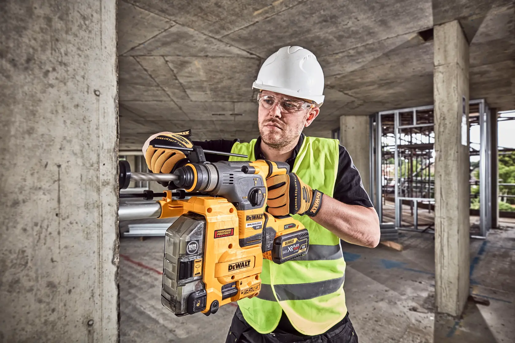 Worker uses a DEWALT DCH335X2 rotary hammer drill on a concrete wall at a construction site.