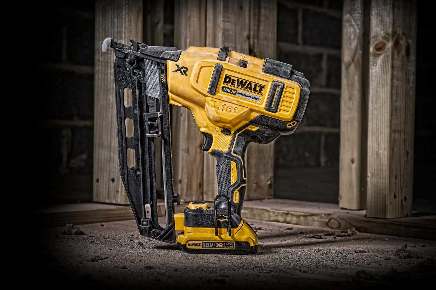 DEWALT 18V cordless nail gun stands on a dusty floor near wooden beams at a construction site.