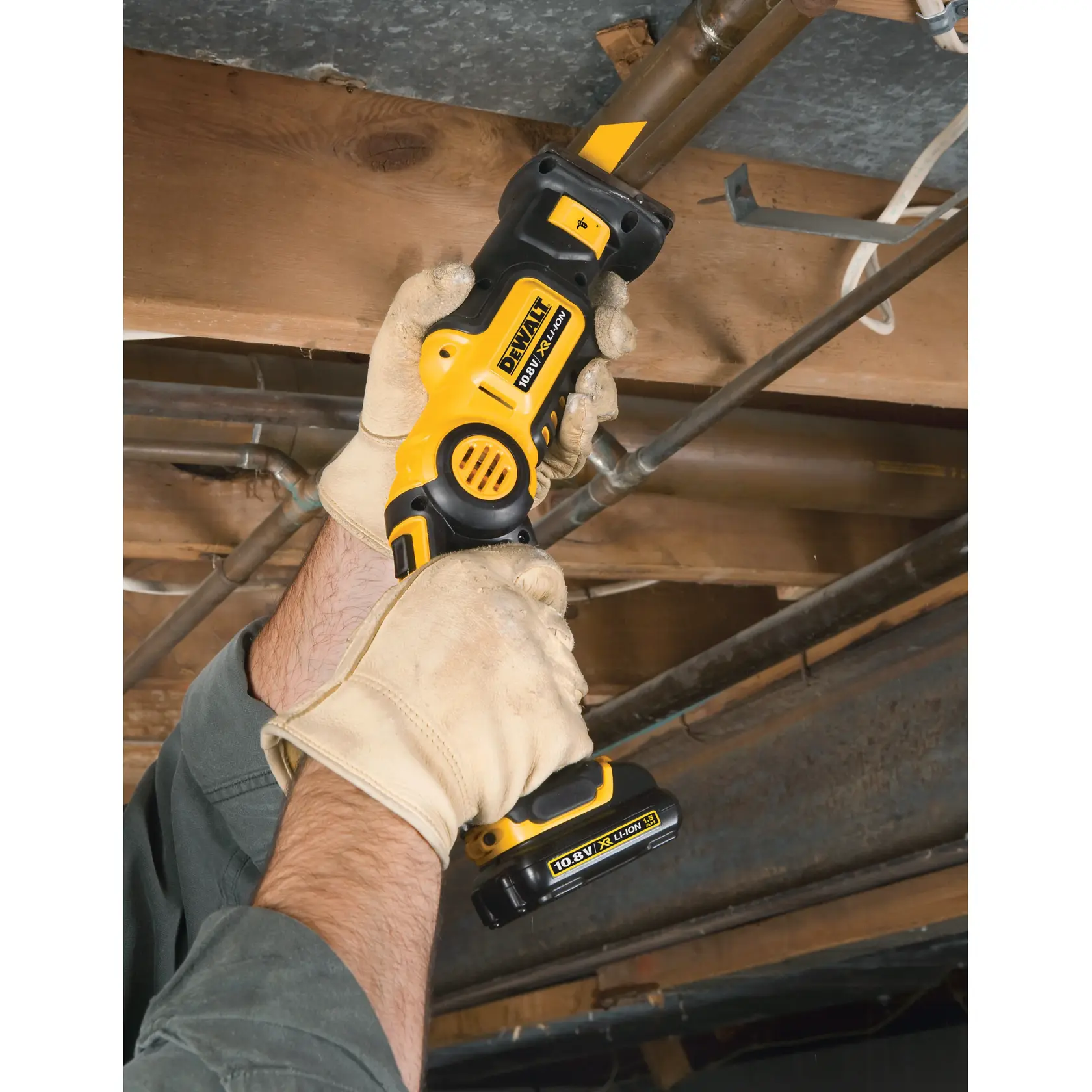 Persona corta un tubo con una sierra DEWALT inalámbrica bajo techo de madera, usando guantes de trabajo.