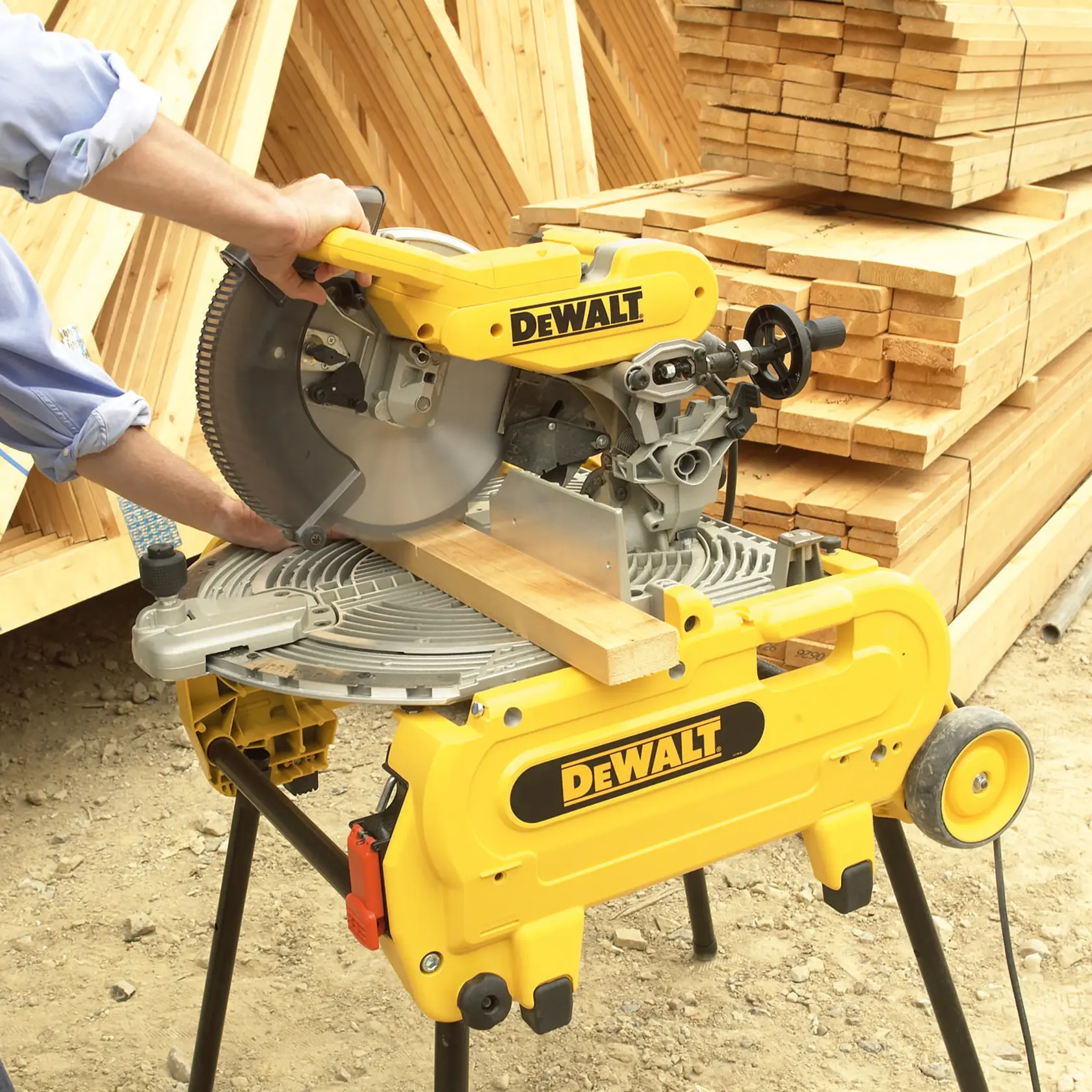 Eine Person bedient eine DEWALT Kappsäge (Modell DT4210), um ein Holzstück zu schneiden. Im Hintergrund befinden sich gestapelte Holzbretter auf einer Baustelle.