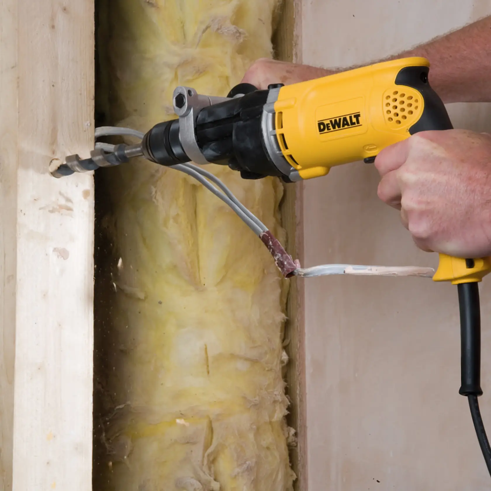 Ein DEWALT-Bohrer bohrt ein Loch in Holz auf einer Baustelle, sichtbare Elektrokabel.