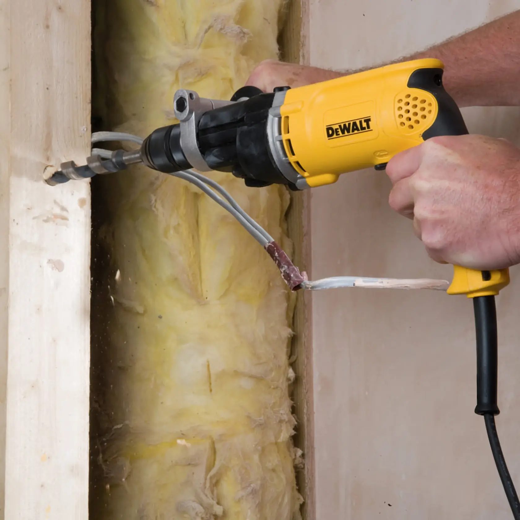 A DEWALT drill is being used to make a hole in wood within a wall, surrounded by insulation and electrical wires.