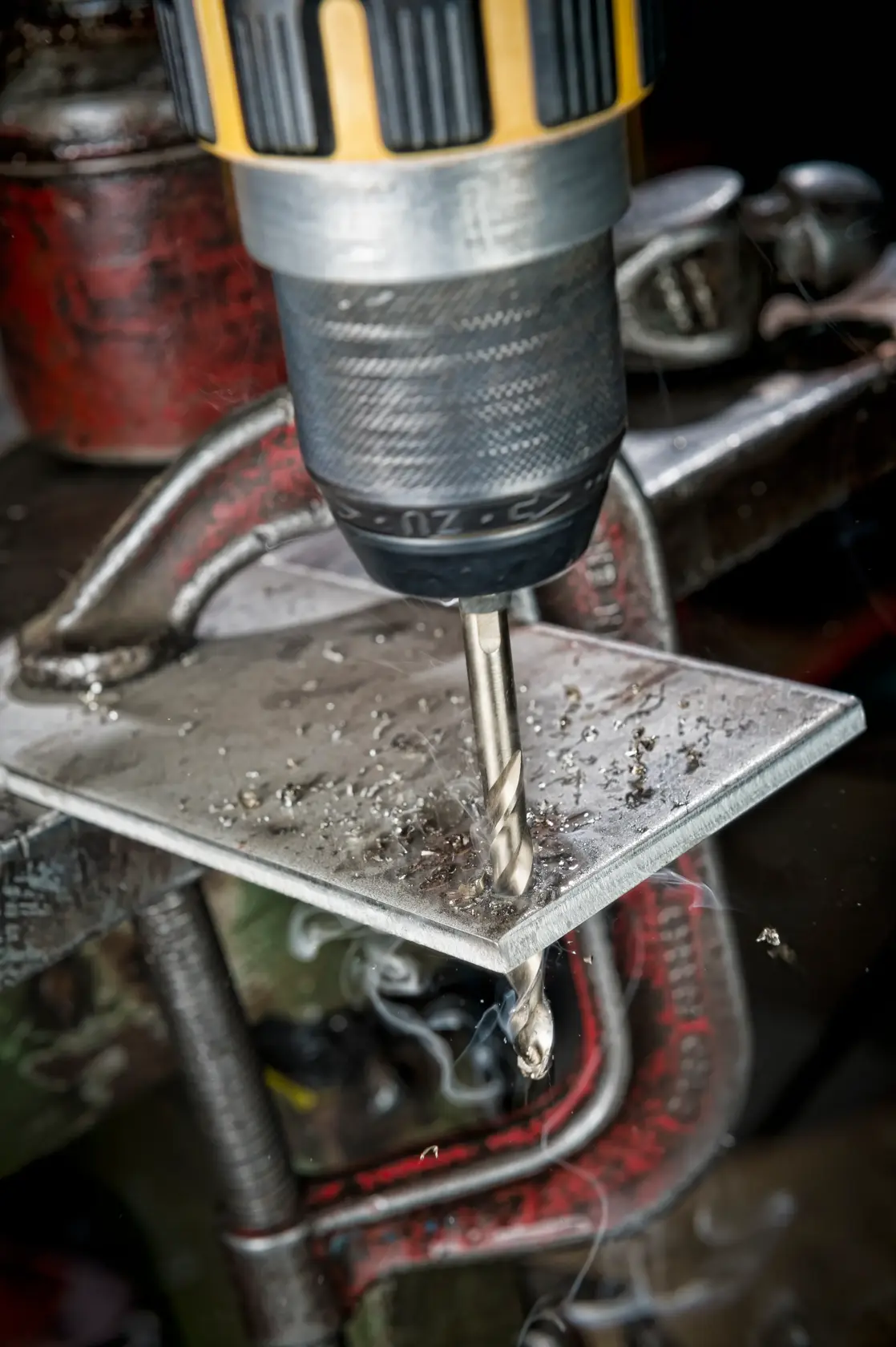 Ein DEWALT-Bohrer durchbohrt ein Metallblech, das mit einer Klammer fixiert ist, mit Metallspänen.