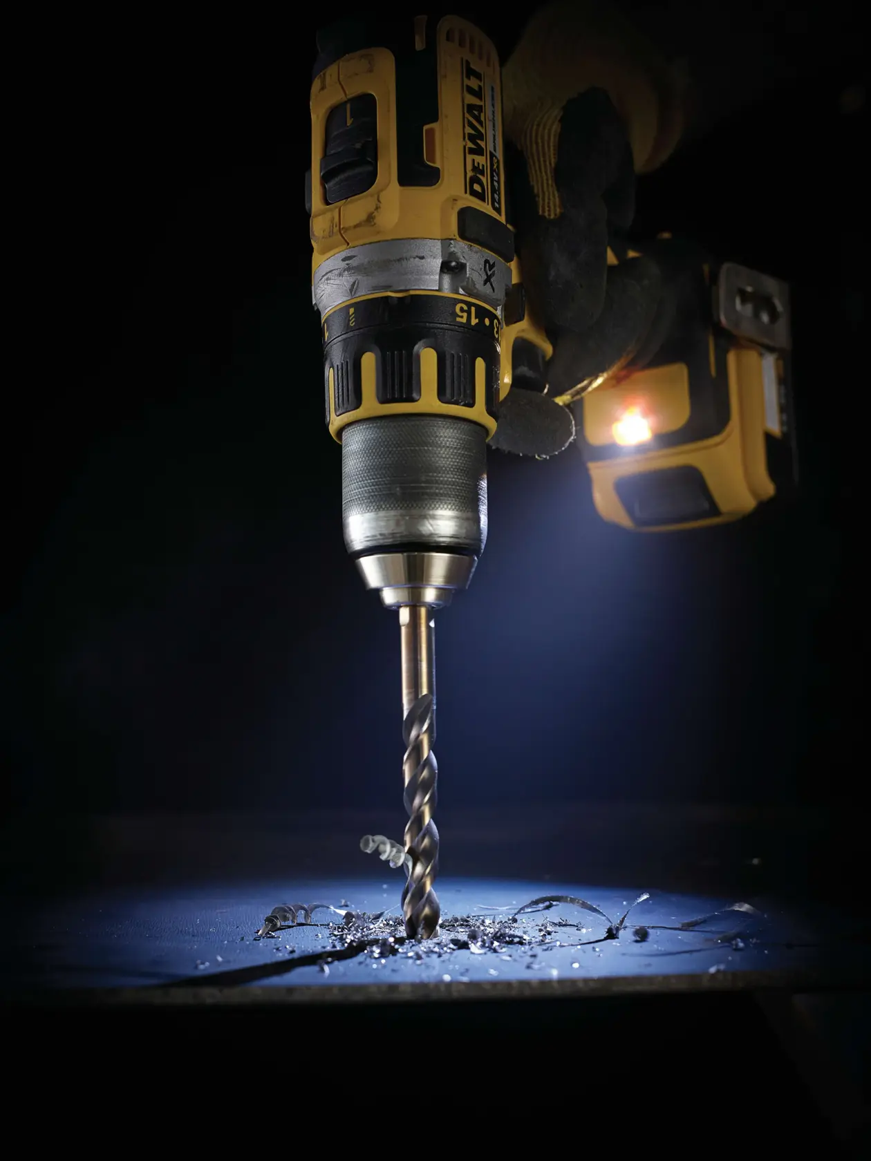 DEWALT-Bohrer im Einsatz, bohrt Metall mit sichtbaren Spänen und einer behandschuhten Hand.