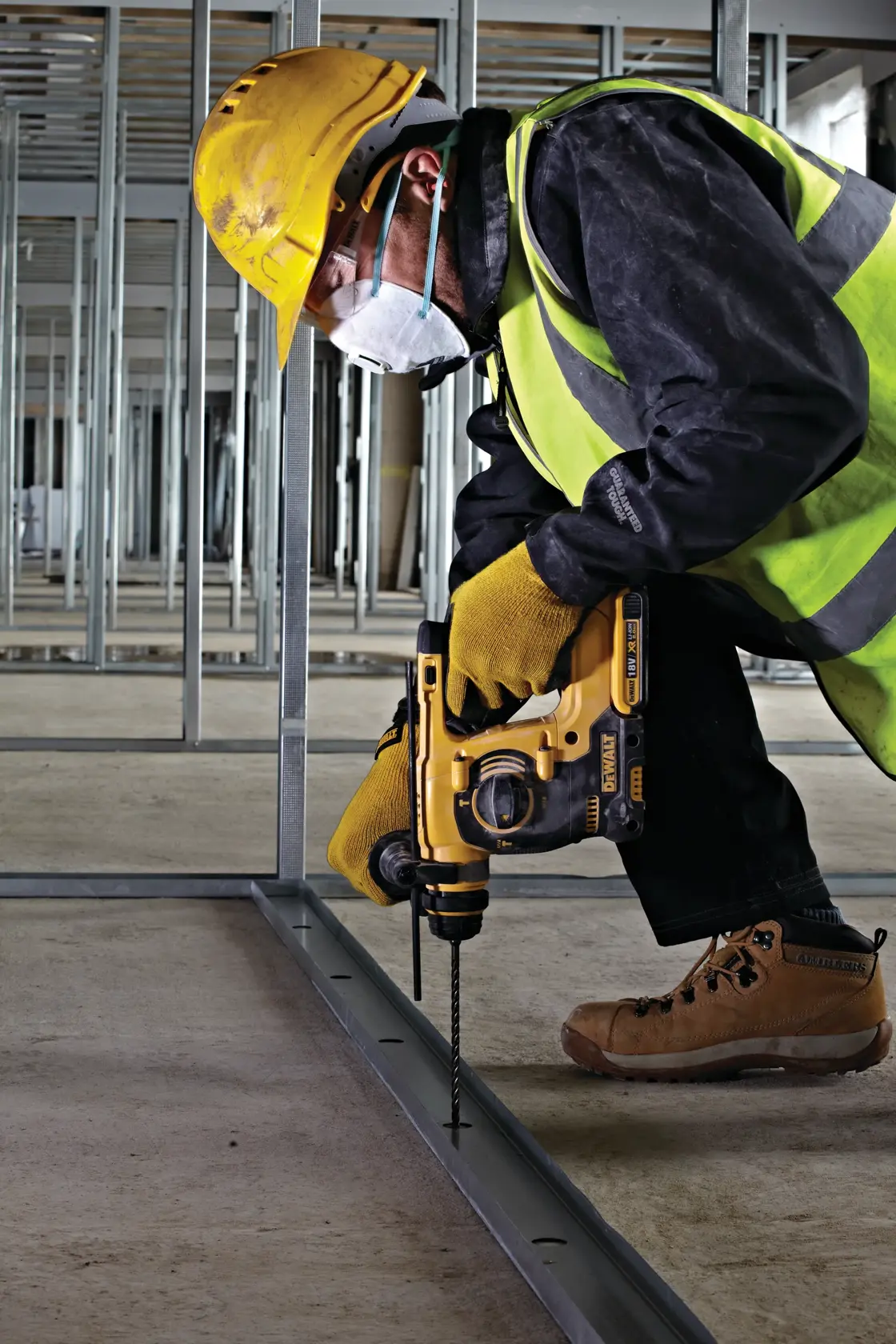 Trabajador usa taladro DEWALT en armazón metálico, con equipo de seguridad y chaleco reflectante en obra.