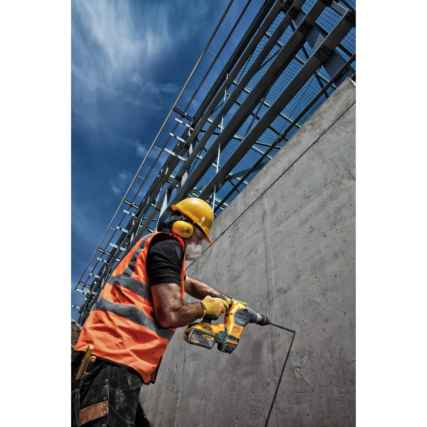 Trabajador perfora muro de concreto con herramienta DEWALT, usando protección y chaleco naranja en obra.
