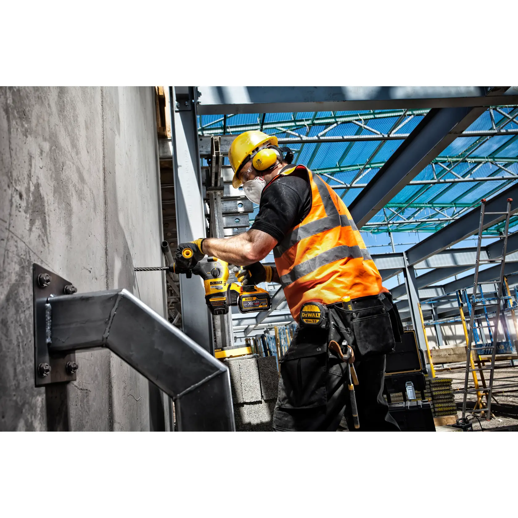 Trabajador usa taladro DEWALT en pared de concreto, lleva equipo de seguridad en un sitio industrial.