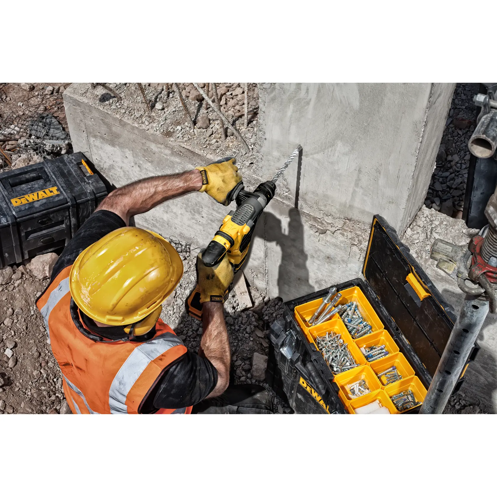 Trabajador taladra pared de concreto con taladro DEWALT. Caja de herramientas cercana en obra.