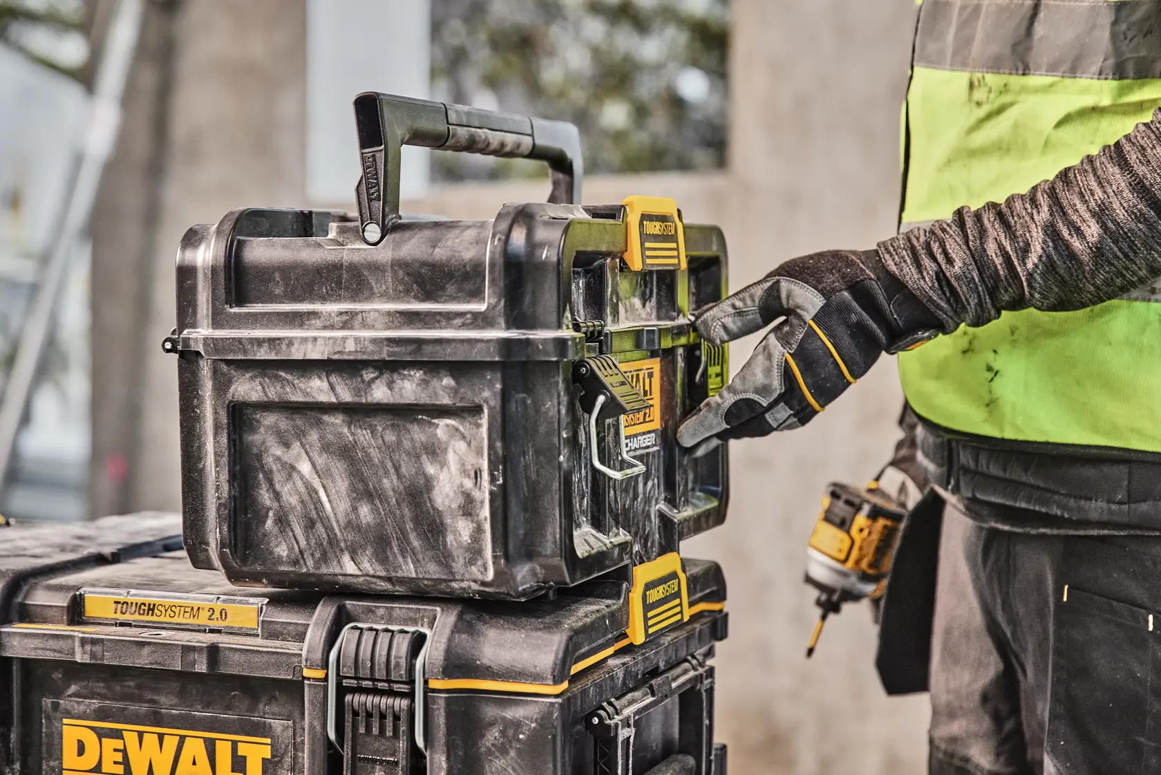 Gloved hand opens DEWALT Toughsystem 2.0 tool box stacked on another box at a worksite.